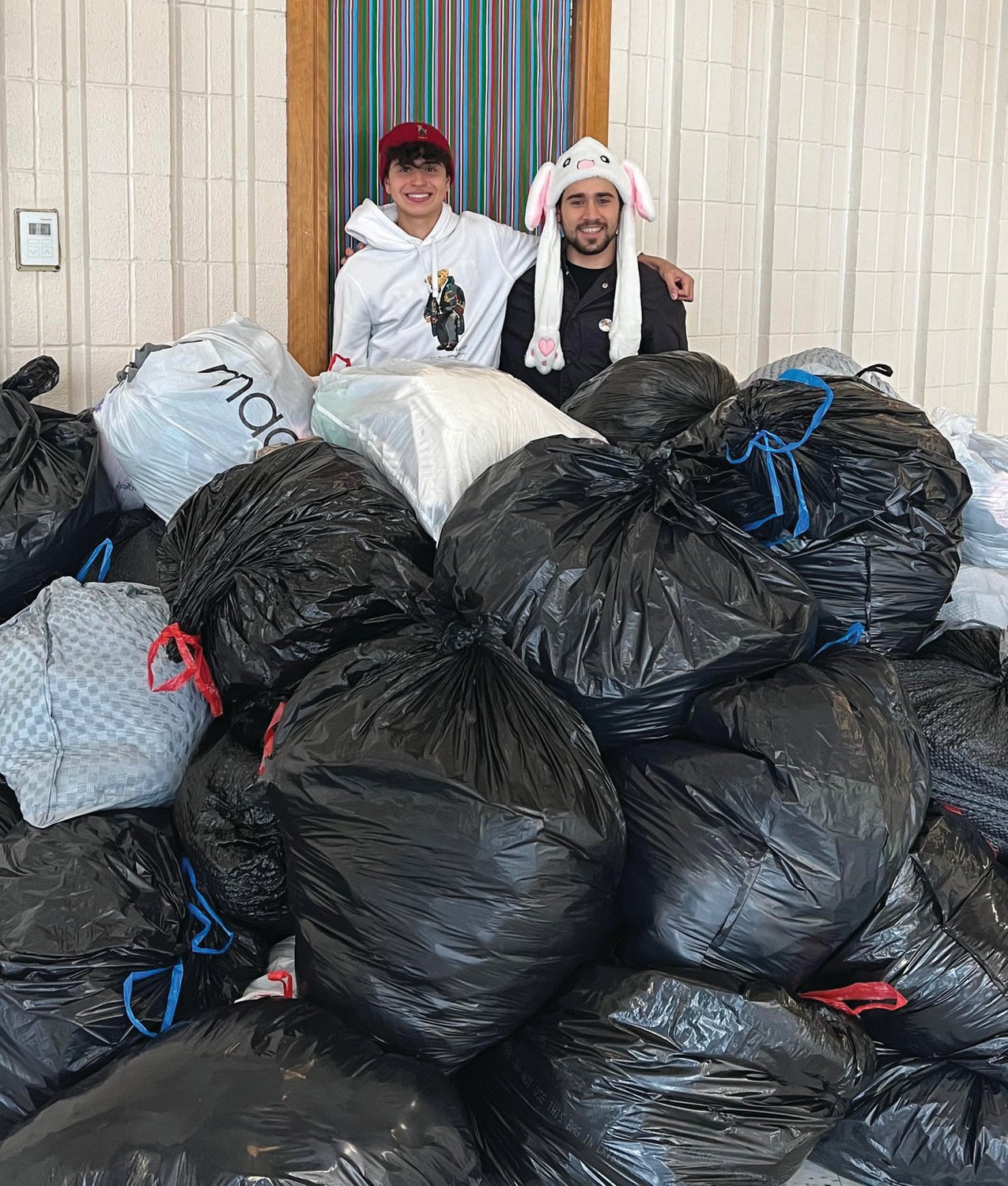 BOUNTIFUL BAGS: JHS music students Kasem Sasa and Mohammed Abaherah, wearing their Crazy Hats, are standing behind one of the many bags filled with gently used clothing that will generate money for the Rachel E. Carson Memorial Scholarships Fund.